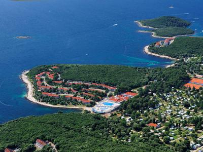 Küste mit Hotelkomplexen, Wald und blauem Meer unter klarem Himmel.