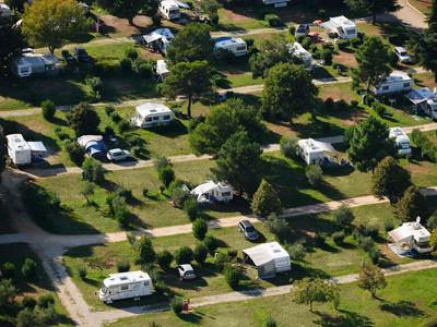 Luftaufnahme eines Campingplatzes mit Wohnmobilen und Zelten in grüner Landschaft.