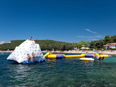 Wasserspielplatz mit Kletterberg und aufblasbaren Hindernissen in klarem Meerwasser bei sonnigem Himmel.