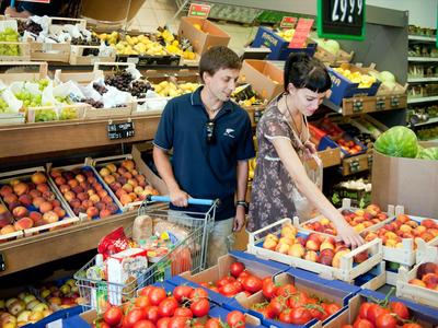 Zwei Personen wählen in einem hellen Supermarkt frisches Obst aus, umgeben von Regalen voller Produkte.