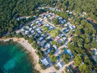 Luftaufnahme eines Hotelresorts am bewaldeten Küstenabschnitt mit Stränden und blauem Wasser.