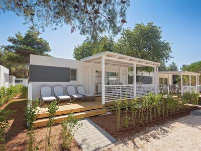 Moderner Bungalow mit Terrasse, Liegen und Gartenbereich unter blauem Himmel.