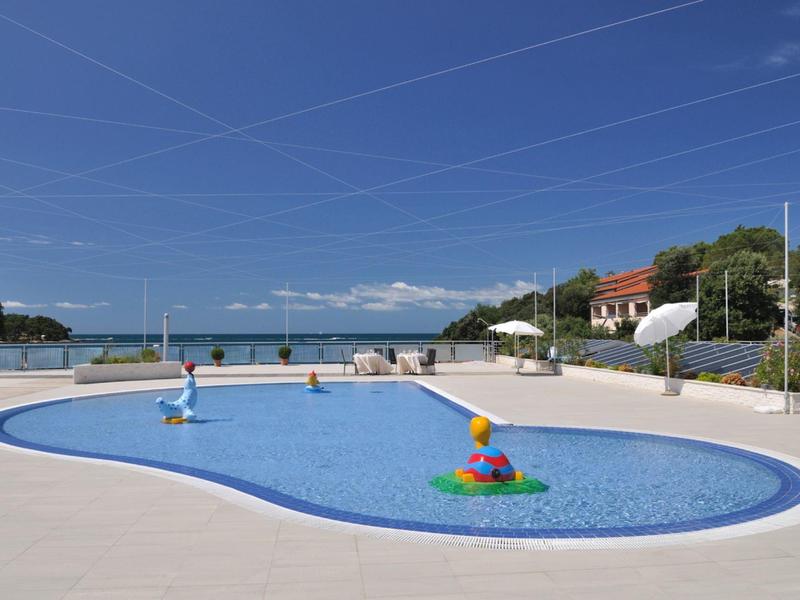 Empty outdoor pool with colorful water toy under clear sky and sea view.