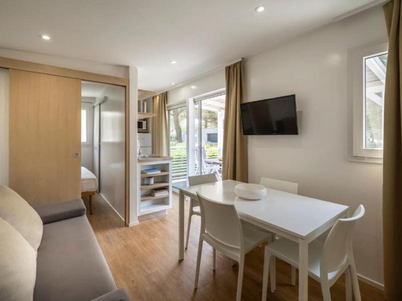 Bright hotel room with dining area, sofa, and balcony overlooking greenery.