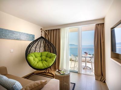 Moderner Raum mit Korbschaukel, grünem Sitzkissen, Sofa, Glastisch und Balkon mit Meerblick.