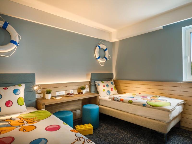 Kleines Schlafzimmer mit zwei Einzelbetten, bunten Bettwäsche und blauen Wänden.