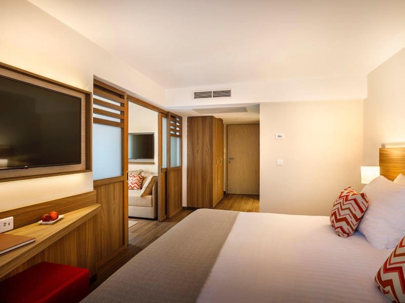 Helles Hotelzimmer mit großem Bett, Holzvertäfelung und Flachbildfernseher an weißer Wand.