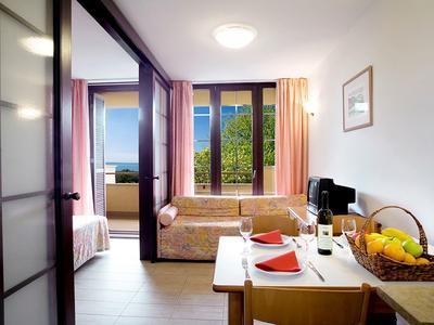 Chambre d'hôtel confortable avec balcon, coin repas et canapé-lit dans un cadre lumineux.