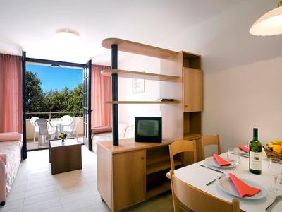 Chambre d'hôtel lumineuse avec balcon, table à manger, canapé, TV et mobilier en bois moderne.