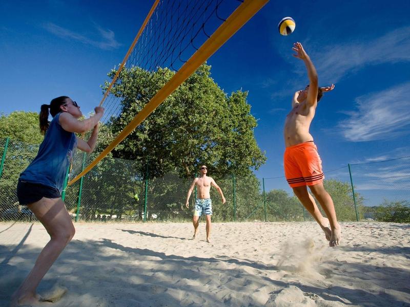 Quatre personnes jouent au beach-volley sur le sable par temps ensoleillé.