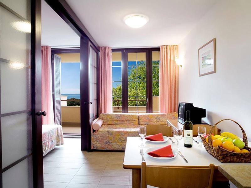 Chambre d'hôtel confortable avec balcon, coin repas et canapé-lit dans un cadre lumineux.