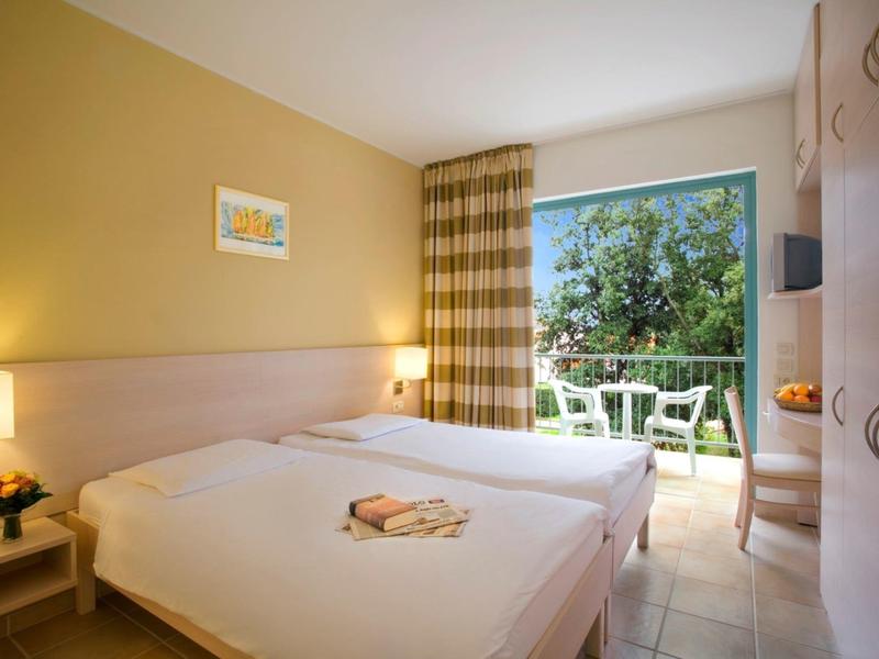 Chambre d'hôtel lumineuse avec deux lits simples, balcon et vue sur la verdure.