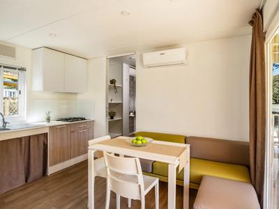 Heller Essbereich mit Holzmöbeln, gelber Sitzbank, weißem Tisch und Klimaanlage an der Wand.