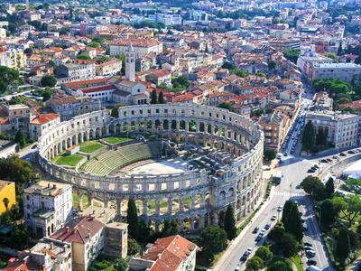 Aerial view of the ancient Roman amphitheater in a city with surrounding buildings and roads.