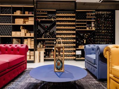 Przytulna część wypoczynkowa z kolorowymi sofami i regałami na wino w tle.