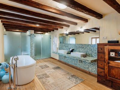 Nowoczesna łazienka z wolnostojącą wanną, drewnianymi belkami sufitowymi i dużymi lustrami.