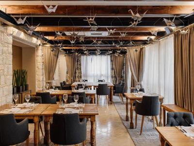 Elegancka restauracja z drewnianymi stołami, czarnymi krzesłami i dużymi zasłoniętymi oknami.