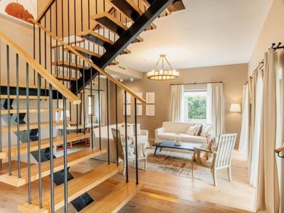Jasny salon z drewnianymi schodami i przytulnym miejscem do siedzenia przy oknie.