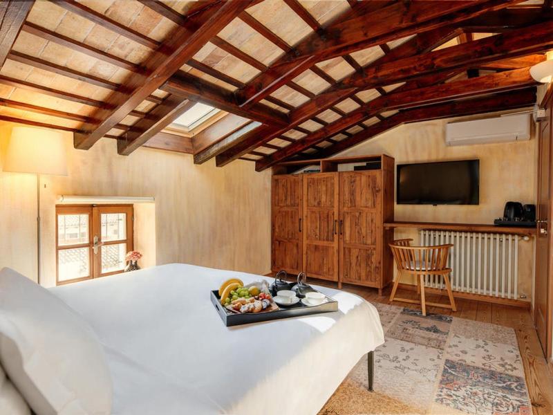 Przytulny pokój na poddaszu z drewnianymi belkami, łóżkiem podwójnym, telewizorem, szafą i oknem.