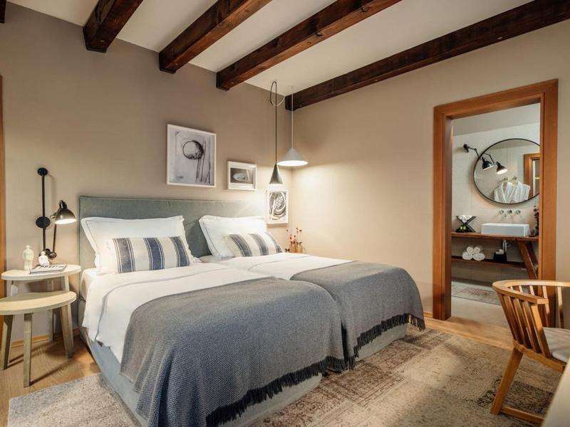 Przytulna sypialnia z podwójnym łóżkiem, drewnianym sufitem z belkami i ciepłymi meblami drewnianymi.