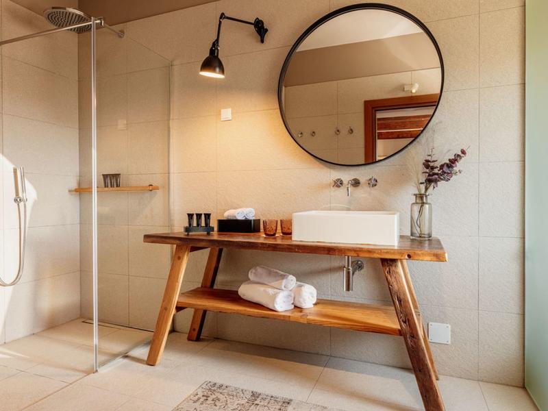 Nowoczesna łazienka z drewnianą umywalką, okrągłym lustrem i prysznicem walk-in.