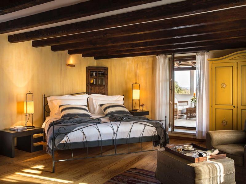 Przytulny pokój hotelowy z drewnianym sufitem belkowym, dużym łóżkiem i wygodnym miejscem do siedzenia.