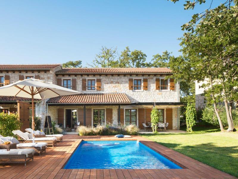 Nowoczesny dom wakacyjny z basenem, leżakami i parasolem w słonecznym ogrodzie.