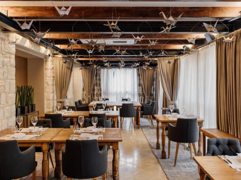 Elegancka restauracja z drewnianymi stołami, czarnymi krzesłami i dużymi zasłoniętymi oknami.