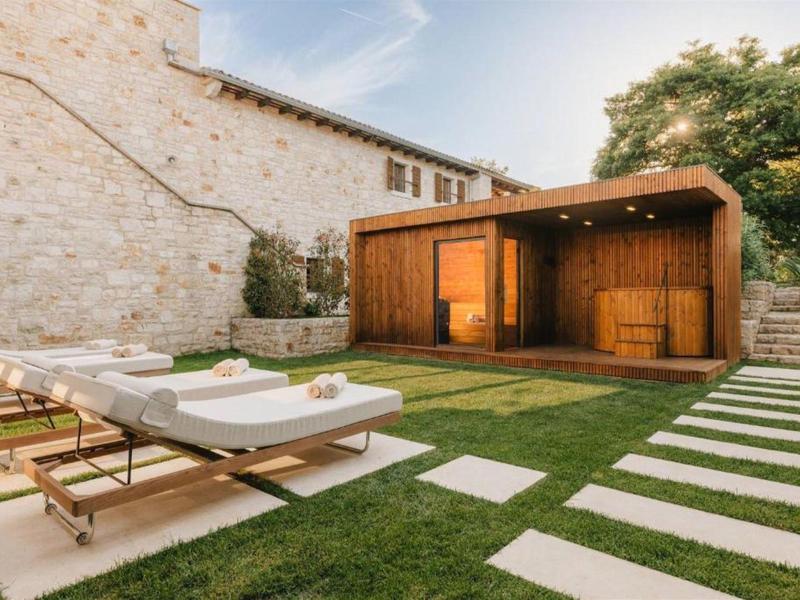 Nowoczesny ogród z drewnianą sauną i leżakami obok kamiennego domu o zachodzie słońca