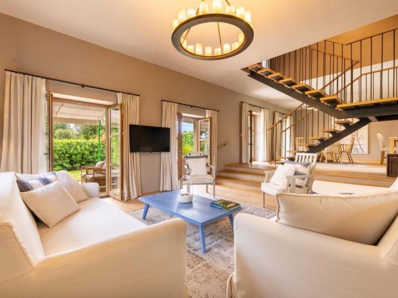 Jasny salon z białymi sofami, niebieskim stołem i otwartymi schodami w nowoczesnym domu.