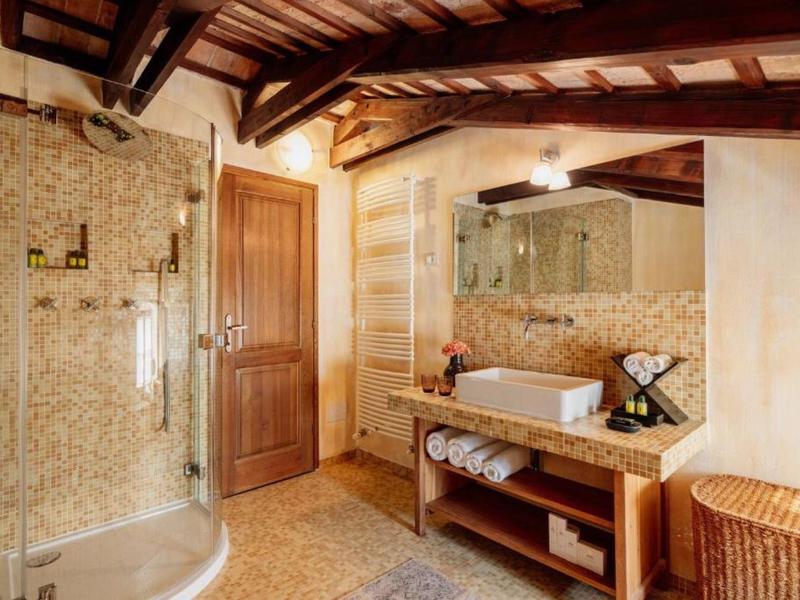 Jasna łazienka z drewnianymi belkami, prysznicem, umywalką na marmurowym blacie i plecionym koszem na pranie.