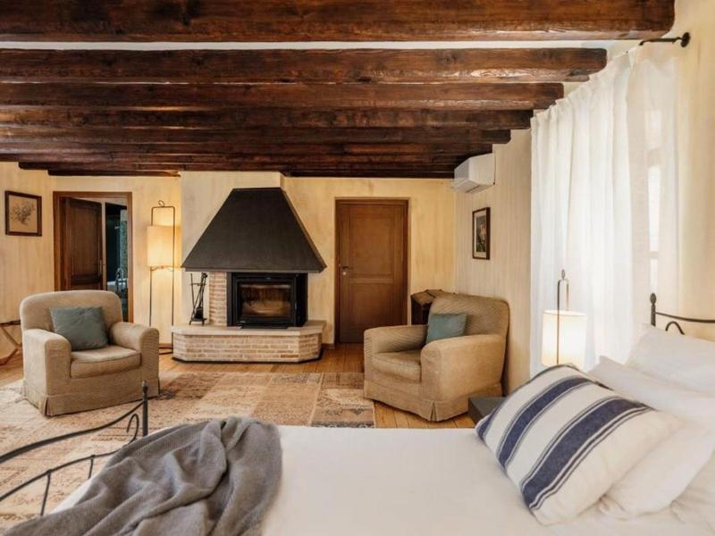 Przytulna sypialnia z drewnianym sufitem, kominkiem i wygodnymi fotelami.