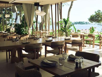 Otevřená restaurace s dřevěnými stoly a výhledem na vodu a stromy.