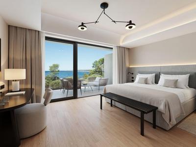 Modern hotel room with large bed, desk, and view of terrace and sea.
