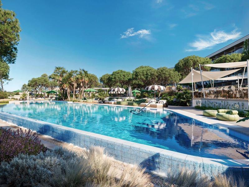 Large hotel pool with loungers and umbrellas under blue sky