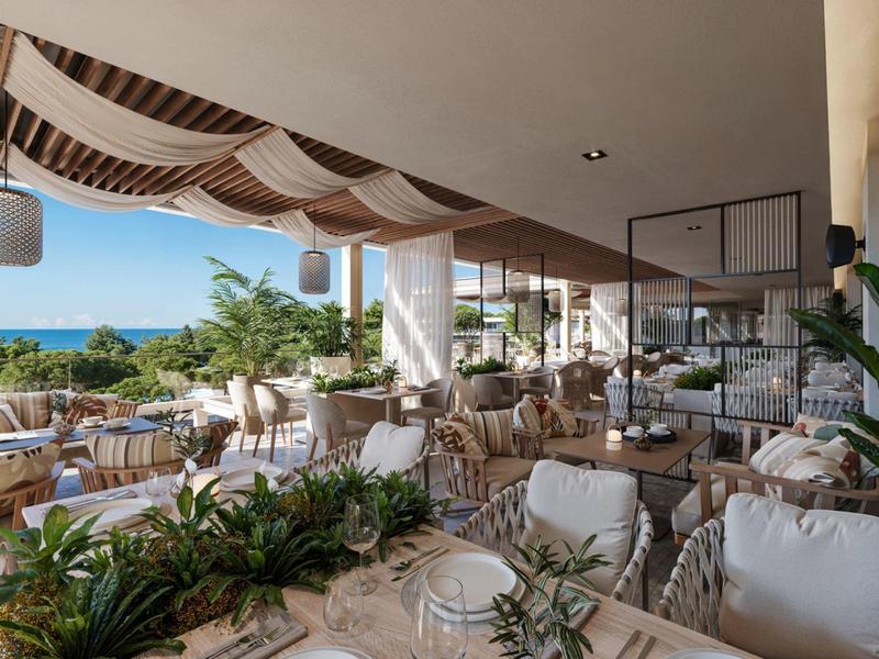 Open restaurant area with set tables, plants, and a sea view near cliffs.