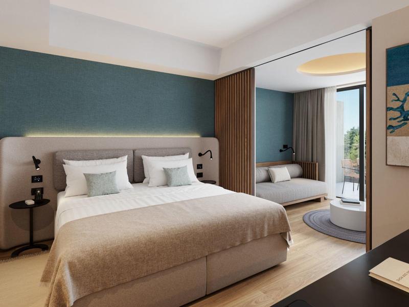 Modern hotel room with large double bed, seating area, and window overlooking the city.