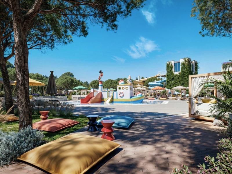 Hotelzwembad met kussens, parasols en bomen bij zonnig weer.