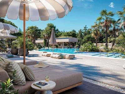 Área de piscina con tumbonas, sombrillas y vegetación exuberante bajo cielo despejado.