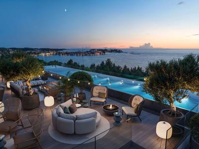 Terraza moderna de hotel con zonas de estar y piscina infinita con vistas al mar al atardecer.