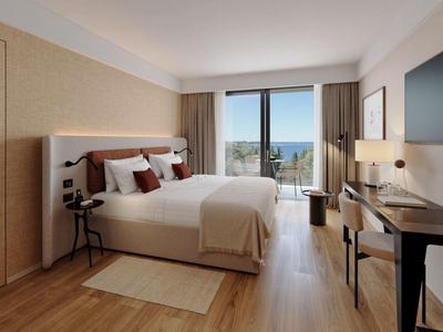 Modernes Hotelzimmer mit Doppelbett, Schreibtisch, Fernseher und Balkon mit Meerblick.