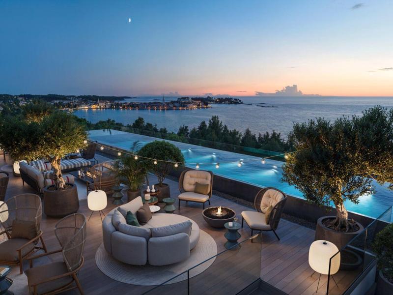 Terrasse mit Sitzmöbeln, beleuchteten Lampen und Infinity-Pool mit Meerblick bei Sonnenuntergang