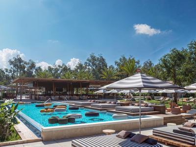 Moderner Außenpoolbereich mit Sonnenliegen und Sonnenschirmen unter blauem Himmel.