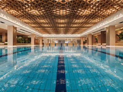 Duży basen kryty z niebieską wodą i dekoracyjnym sufitem w luksusowym hotelu