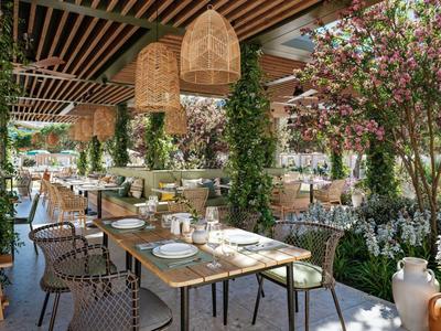 Jasno urządzona duża zewnętrzna część restauracji z wieloma roślinami i wiszącymi lampami.