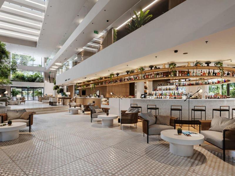 Nowoczesny bar hotelowy z miejscami do siedzenia, roślinami i naturalnym światłem przez szklany dach.