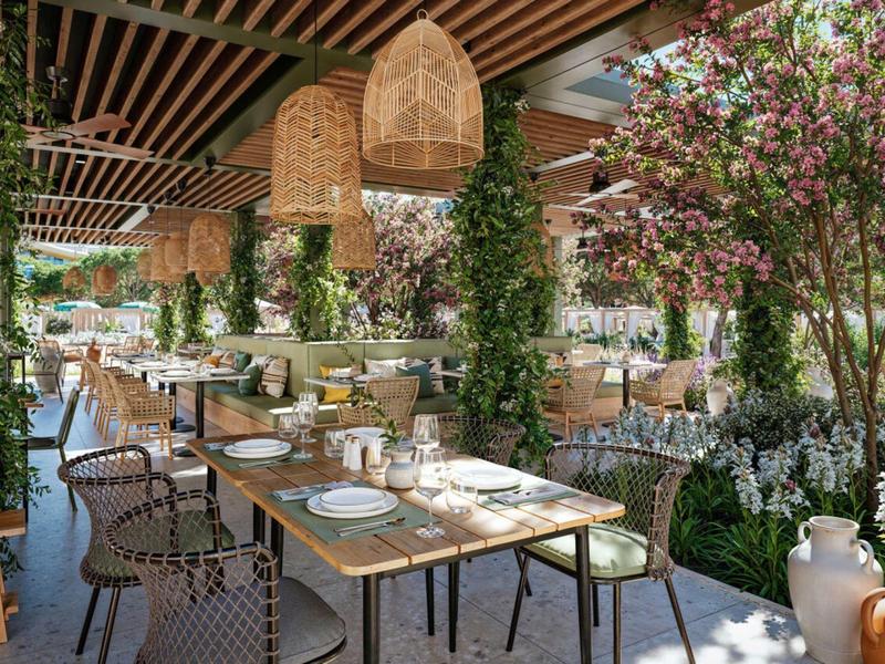 Jasno urządzona duża zewnętrzna część restauracji z wieloma roślinami i wiszącymi lampami.