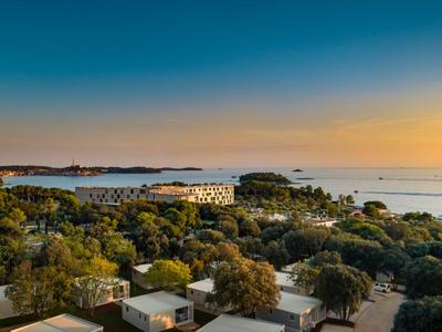 Hotelanlage am Meer mit vielen Bäumen und Sonnenuntergang im Hintergrund.