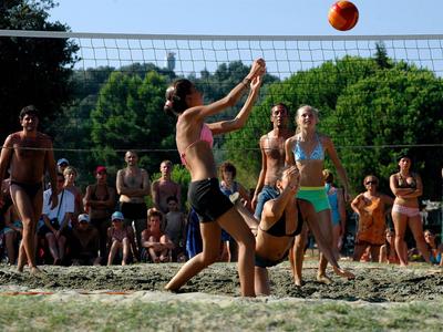 Giovani che giocano a beach volley su un campo di sabbia all'aperto con spettatori sullo sfondo