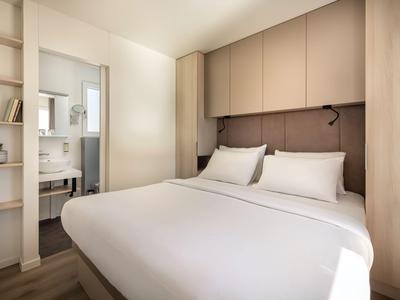 Schlafzimmer mit großem Bett, weißen Kissen, Holzschränken und minimalistischer Einrichtung.